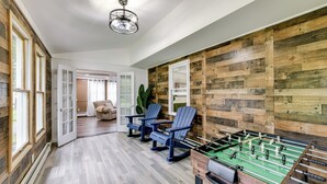 Ein Zimmer mit einer Holzwand, einem Tischkicker und drei blauen Adirondack-Stühlen.