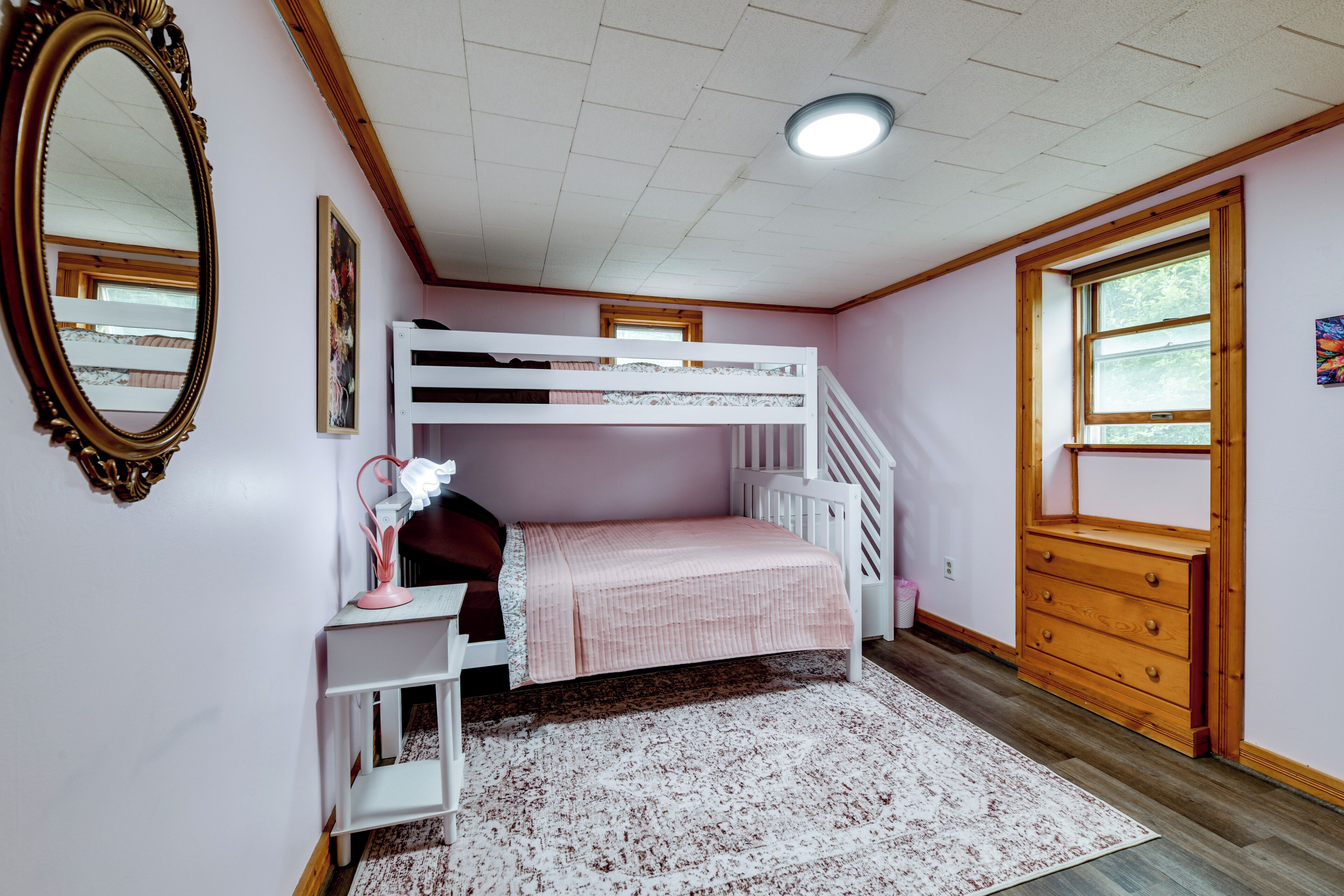 A bedroom with a bunk bed, a dresser, a mirror, and a window.