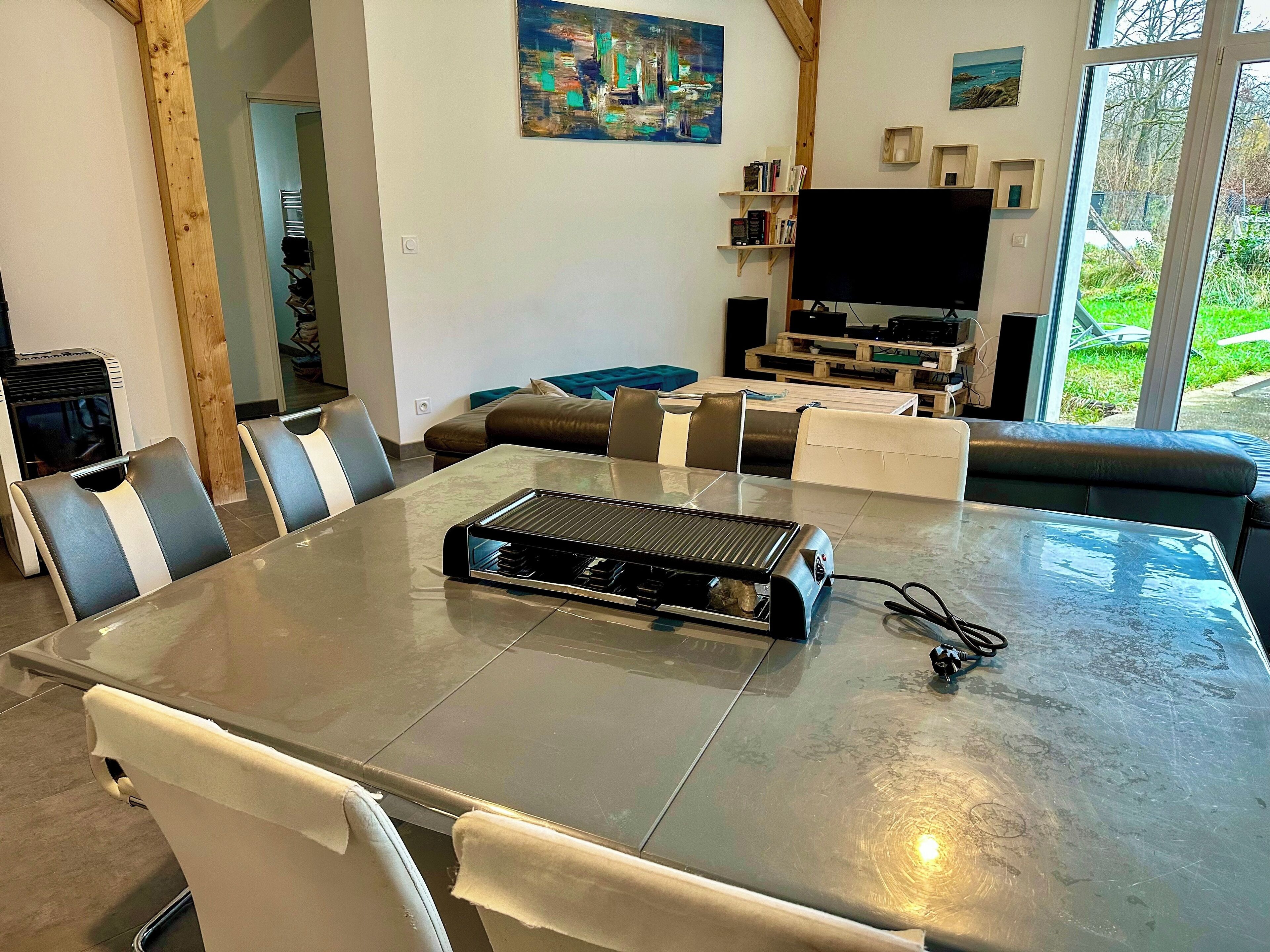 A modern living room with a dining area, a large window, and a flat-screen TV.