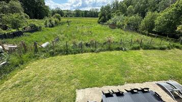 A grassy outdoor area with a fenced garden, a picnic table, and a building with a sloped roof.