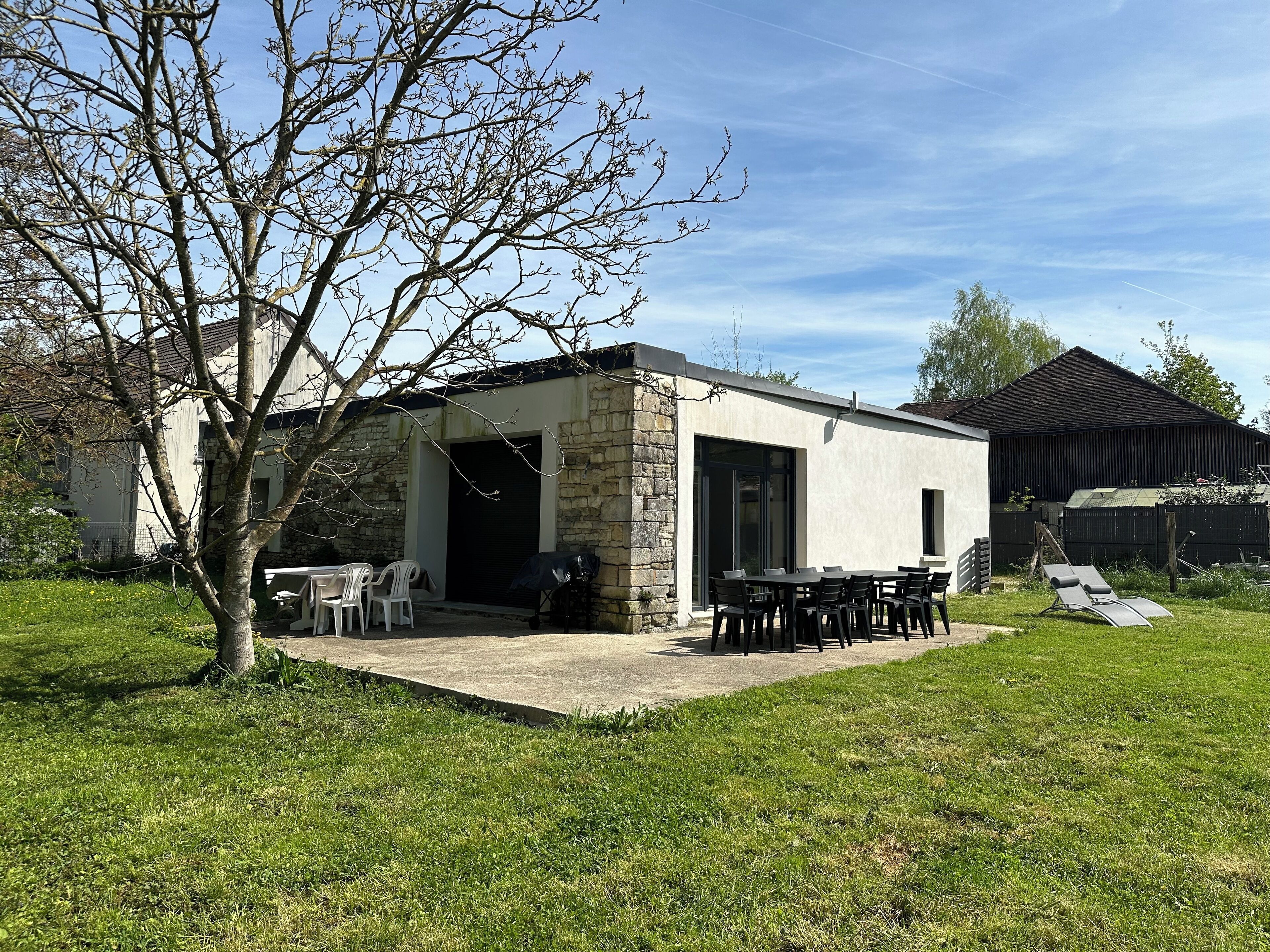 Una casa moderna con fachada de piedra, un patio con mobiliario exterior y un amplio ventanal corredera.