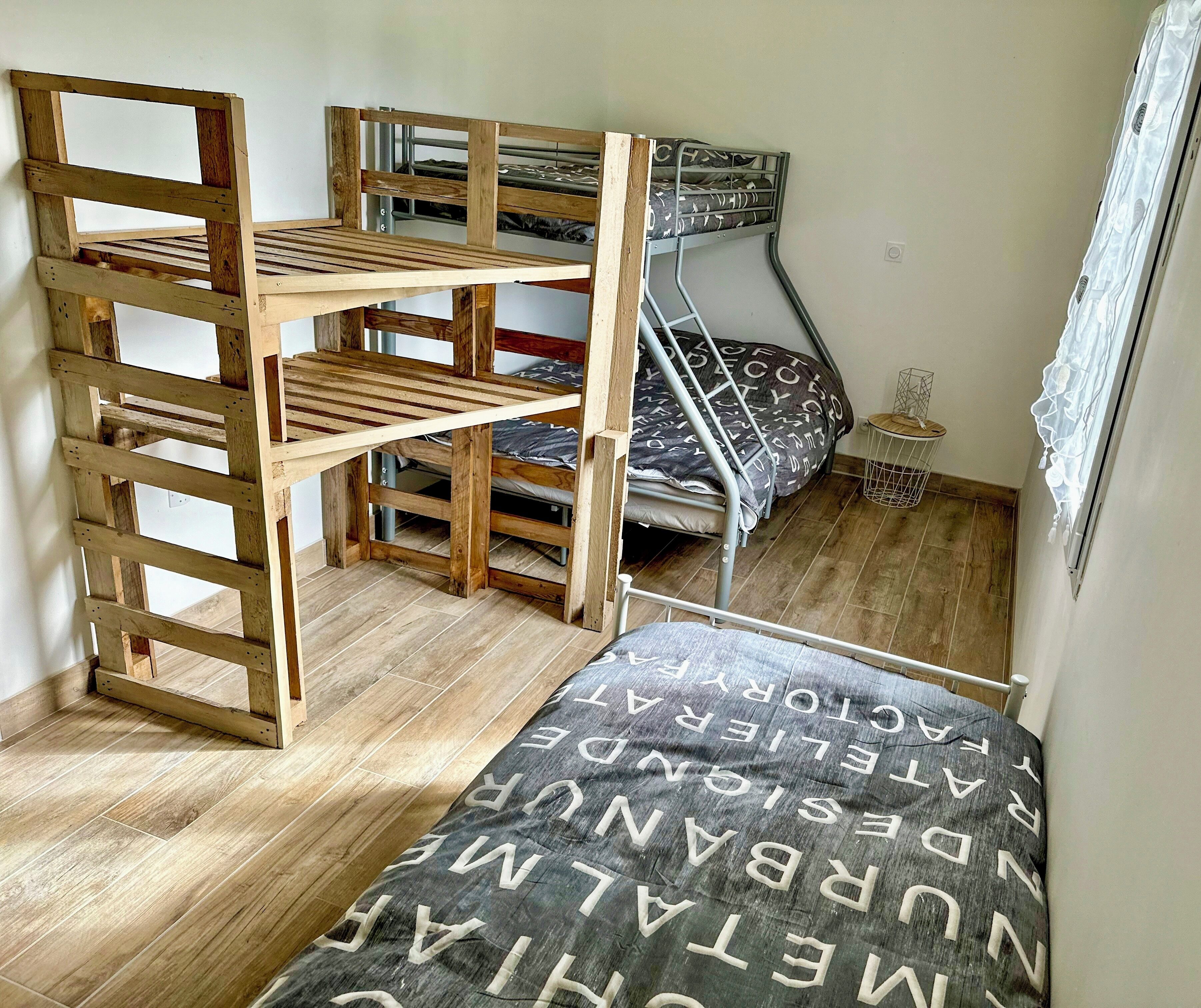 Une pièce avec un lit superposé, une échelle en bois, une petite table et une fenêtre.