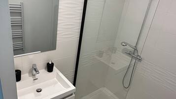 A modern bathroom with a glass-enclosed shower, a white sink with a mirror, and dark wooden flooring.