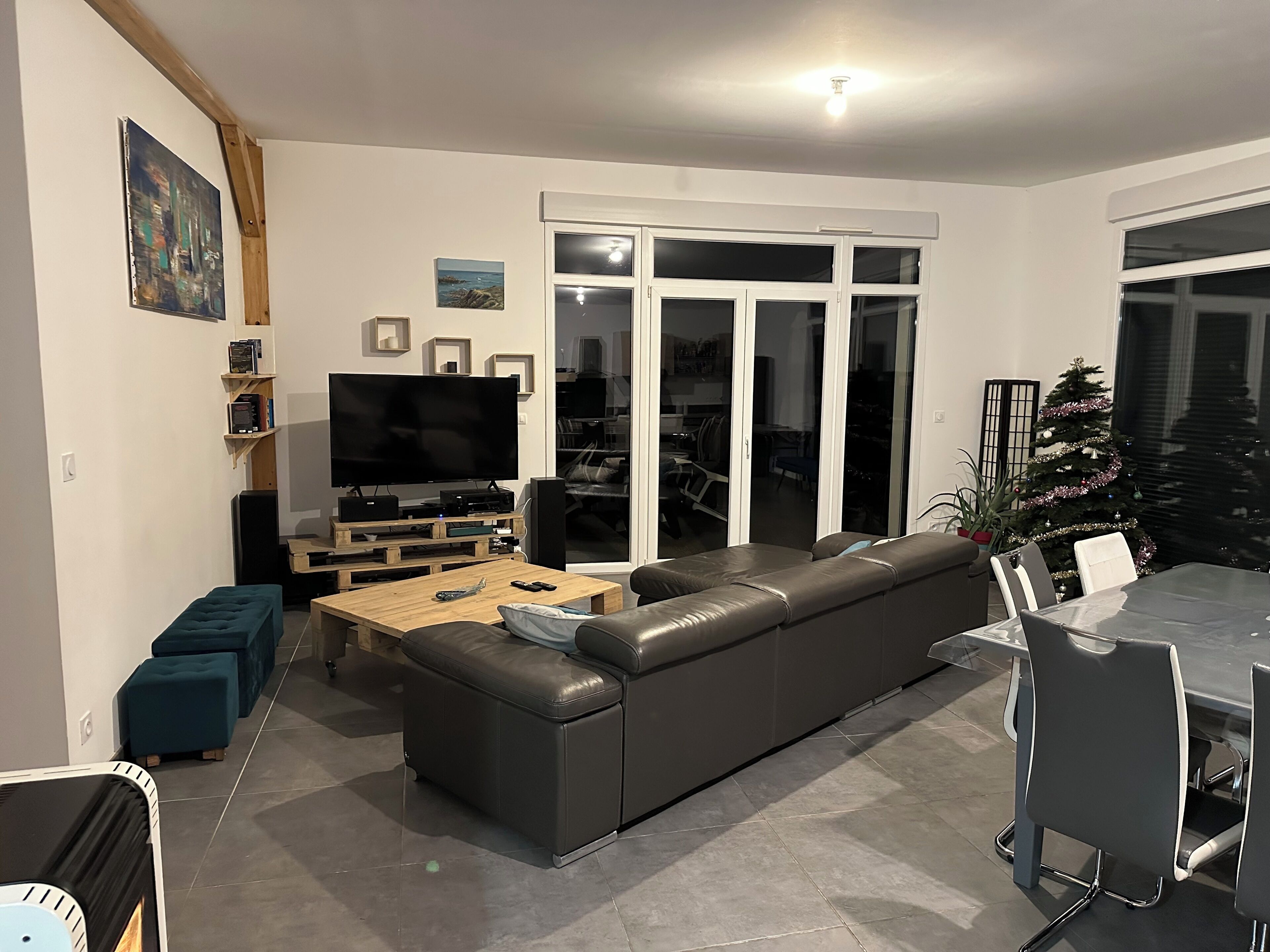 Een moderne woonkamer met een modulaire bank, een flatscreen televisie, een houten salontafel en een eethoek met een glazen tafel en stoelen.