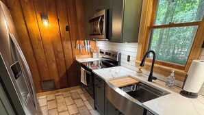 A modern kitchen with wooden walls, a stainless steel refrigerator, a microwave, and a sink with a window above it.