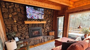 A cozy cabin interior with a stone fireplace, wooden ceiling, and a television mounted on the wall.