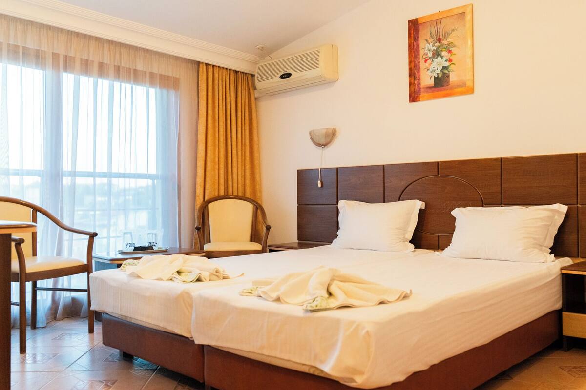 A hotel room with a large bed, two bedside tables, a chair, a desk, and a window with curtains.