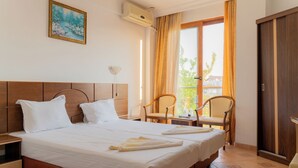 Une chambre d’hôtel avec un lit, deux chaises, une table de chevet, un tableau et une fenêtre avec des rideaux.