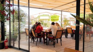 Un café en plein air avec des tables et des chaises, de grandes fenêtres et des plantes en pot.