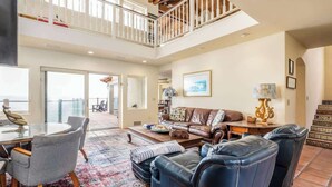 A spacious living area with a high ceiling, a balcony, a dining area, and a seating arrangement.