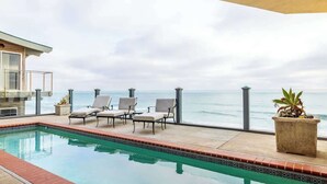 An indoor swimming pool with a view of the ocean, surrounded by lounge chairs and a potted plant.