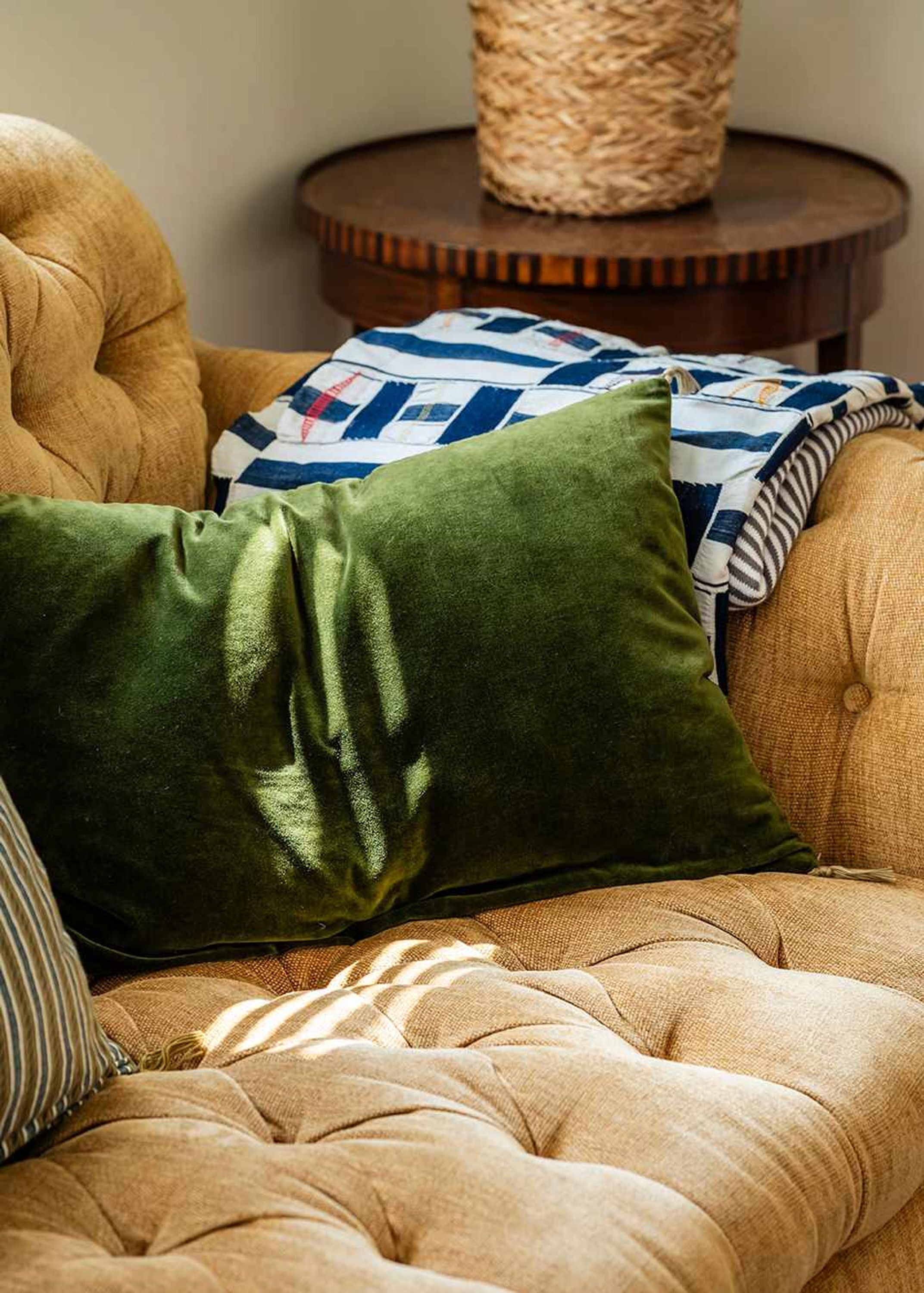 A tufted armchair with a green pillow and a patterned throw blanket.