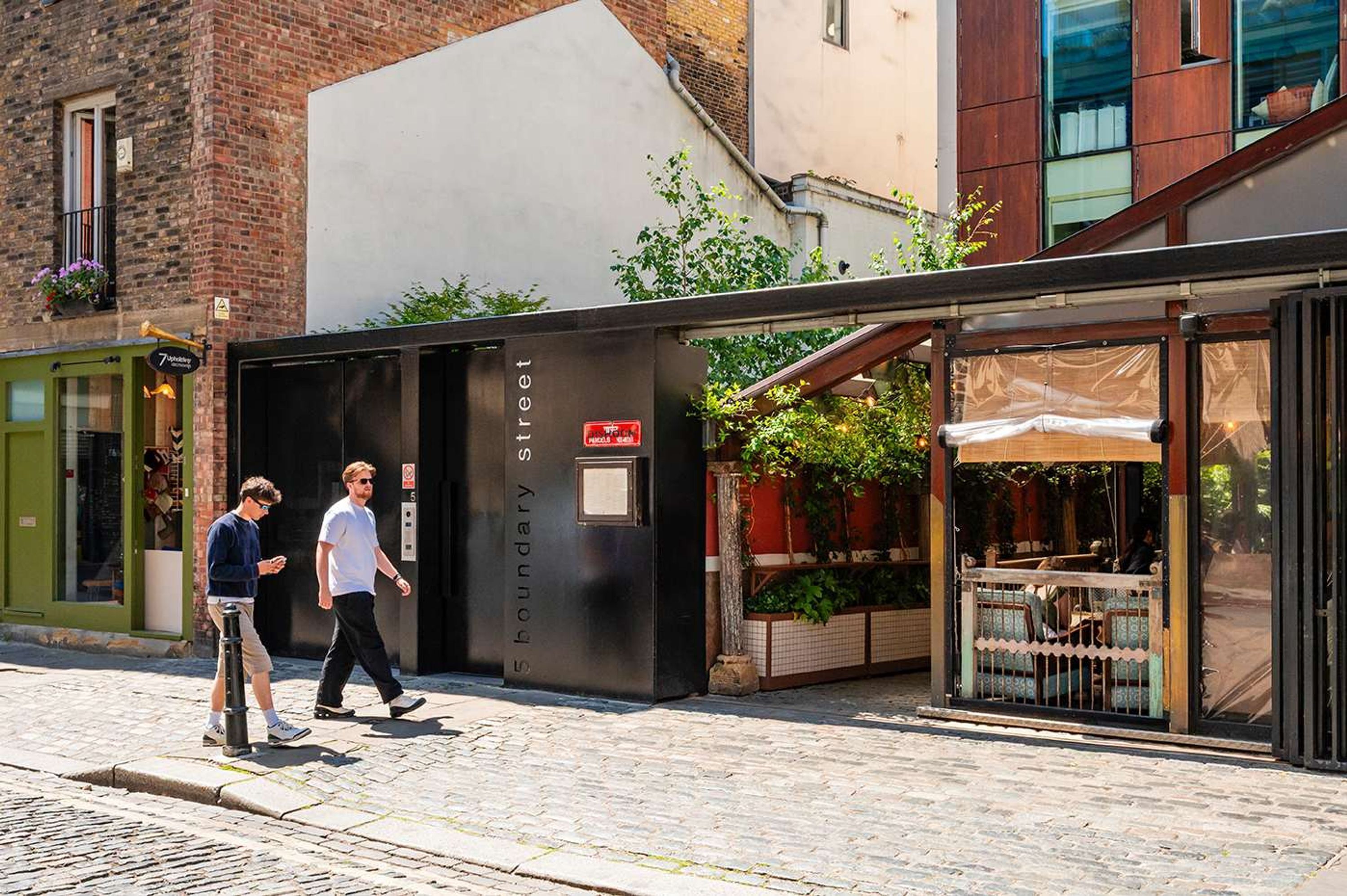 Un bâtiment à la façade noire, une enseigne indiquant « 5, rue Boundary », et un espace extérieur abrité avec des sièges, offrant une vue sur la rue.