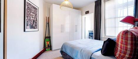 Une chambre d’hôtel moderne équipée d’un lit, d’un bureau, d’une chaise, d’une fenêtre avec des rideaux, d’un luminaire suspendu et d’un tableau encadré au mur.