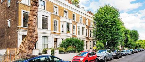 A row of parked cars along a tree-lined street with a row of terraced houses.