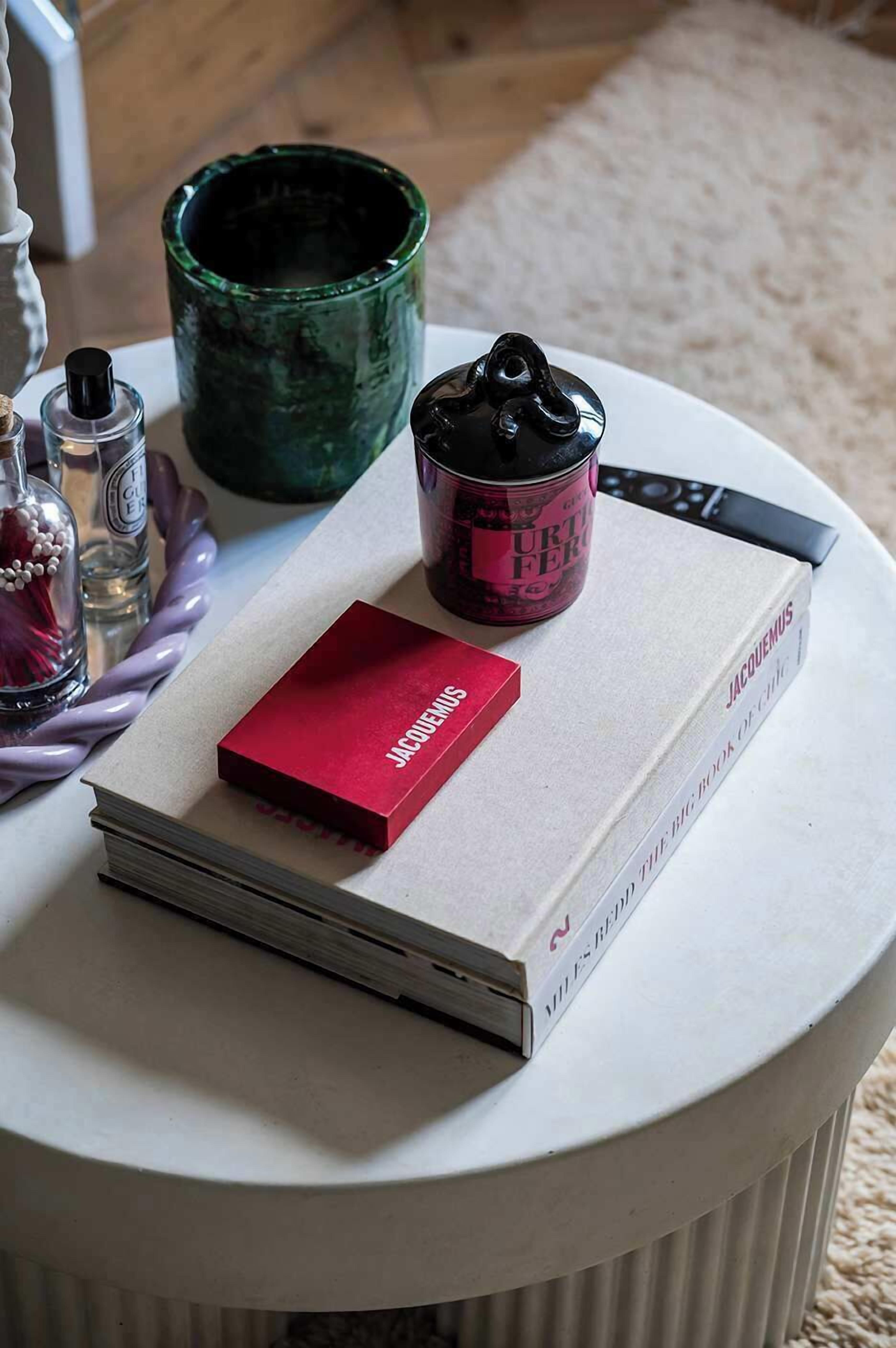 A white round table with a book titled 'JACQUEMUS' and a red box labeled 'JACQUEMUS' on it.