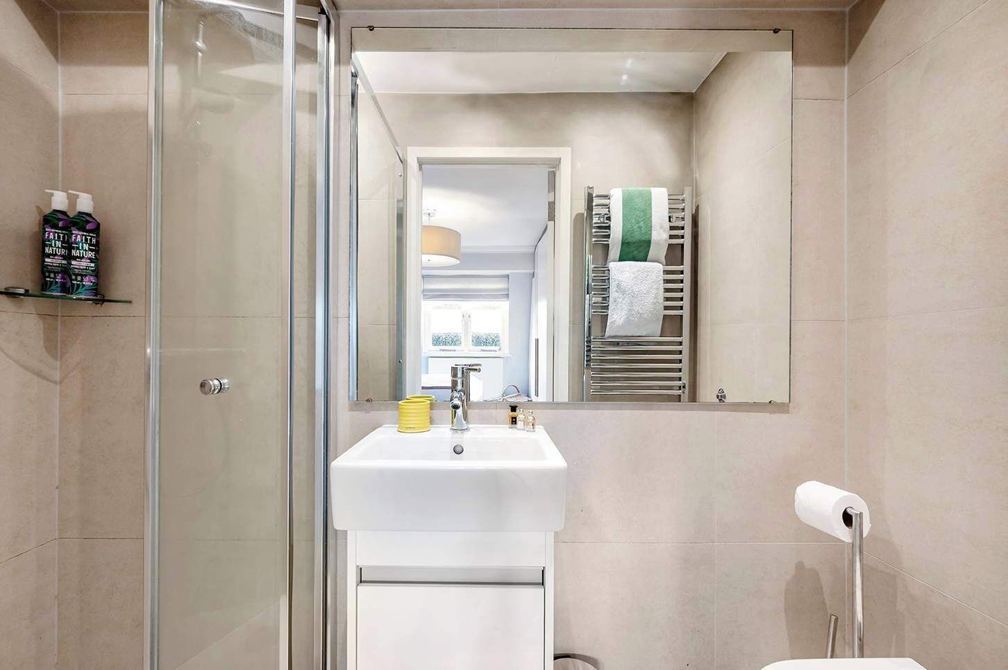 A modern bathroom with a glass shower enclosure, a white sink with a mirror above it, and a towel rack with a green towel.