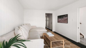 Een moderne woonkamer met een beige bank, een houten salontafel en een grote plant.