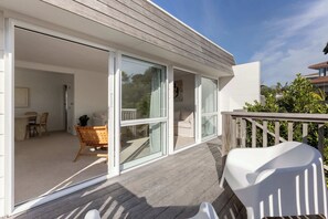 Une maison moderne dotée d’une terrasse en bois et de portes-fenêtres coulissantes qui donnent sur un espace intérieur comprenant un coin repas, un canapé et un fauteuil.