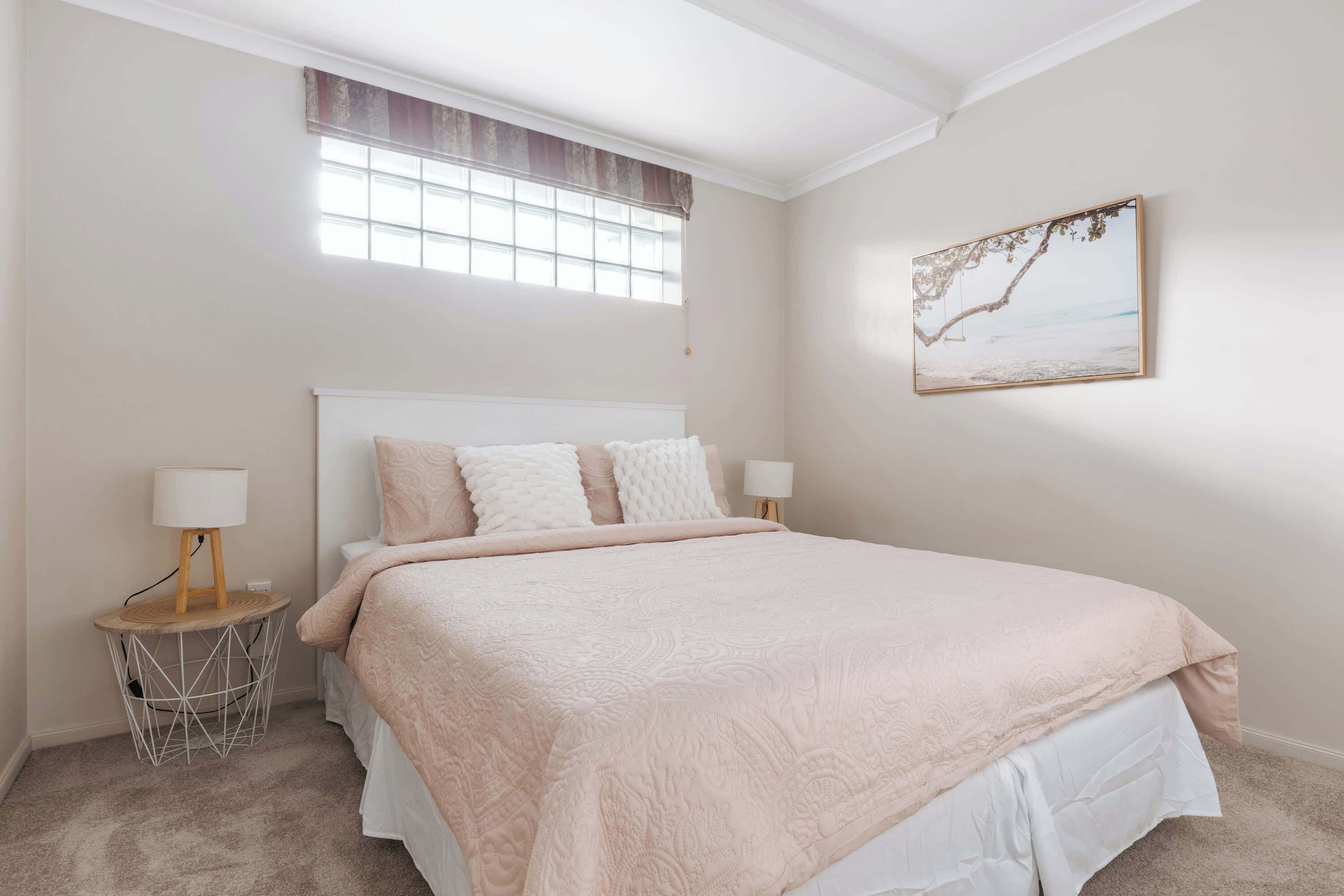 Une chambre avec un grand lit, deux lampes de chevet, une petite table ronde avec une lampe et une fenêtre donnant sur la plage.