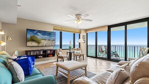 A spacious living room with a large TV, comfortable seating, a ceiling fan, and a balcony with a view of the ocean. - It Doesn’t Get Any Better Than This! 2BR 2BA Sleeps 8 Beachfront! (Panama City Beach)
