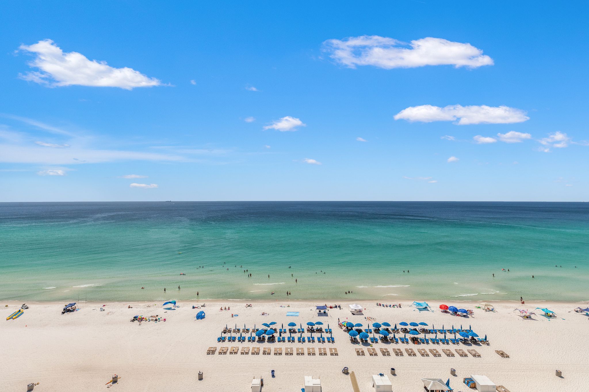 A beach with clear turquoise water, a sandy shore, and several blue umbrellas and sun loungers.