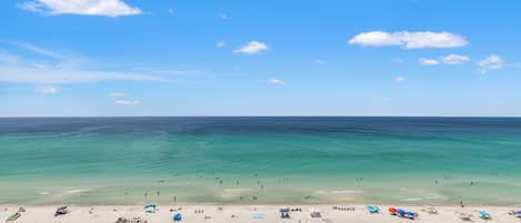 A beach with clear turquoise water, a sandy shore, and several blue umbrellas and sun loungers.