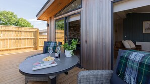 A wooden deck with a table set for two, a wicker chair, and a sofa with a plaid blanket.
