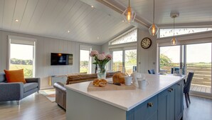 A modern kitchen with a large island, wooden cabinets, and a dining area with a view.
