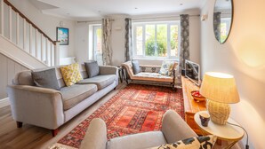 Ein Wohnzimmer mit einer Couch, einem gemusterten Teppich, einer Lampe und Blick ins Freie durch große Fenster.