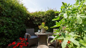 En terrasse med fletningsmøbler, et rundt bord og krukkeplanter.