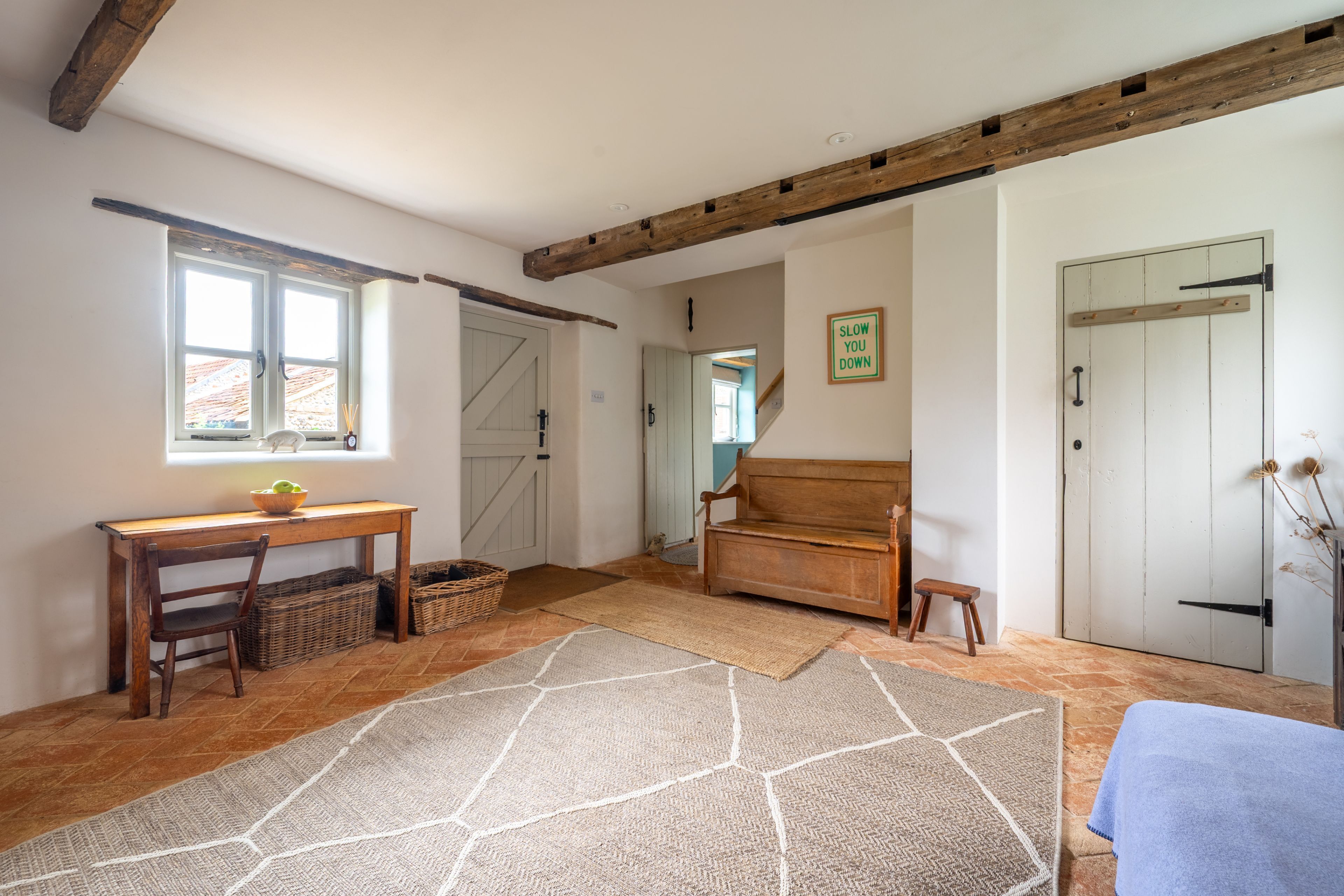 A room with a wooden desk, a bench, a rug, and a door with a 'SLOW YOU DOWN' sign.