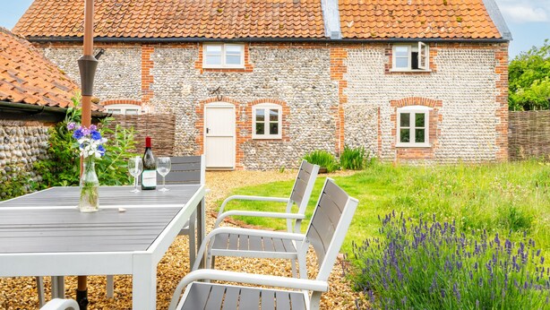 Une maison en pierre avec un toit en tuiles, un jardin agrémenté de lavande et du mobilier d’extérieur.