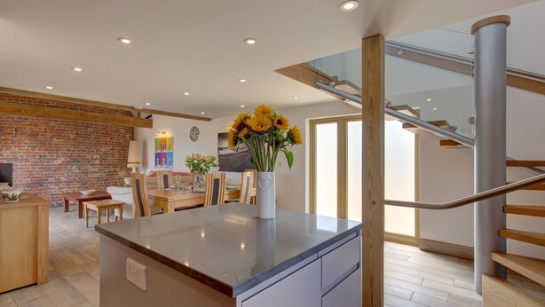 Une cuisine moderne dotée d’un îlot central, d’un coin repas avec des meubles en bois, d’un mur en briques et d’un escalier avec une rampe en verre.