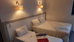 Et hotelværelse med to senge, hver med hvid sengetæppe og puder. Der er vægmonterede lamper på hver side af sengene.