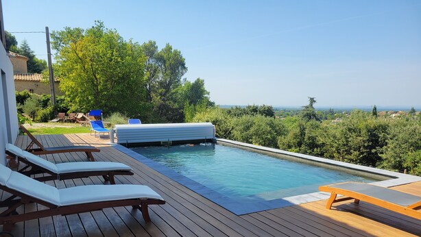 Um deck de madeira com piscina, cadeiras de lounge e vista para a paisagem.
