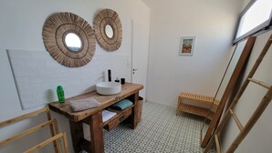 Casa de banho com toucador de madeira, dois espelhos fixados na parede, um quadro emoldurado e soalho em azulejos.