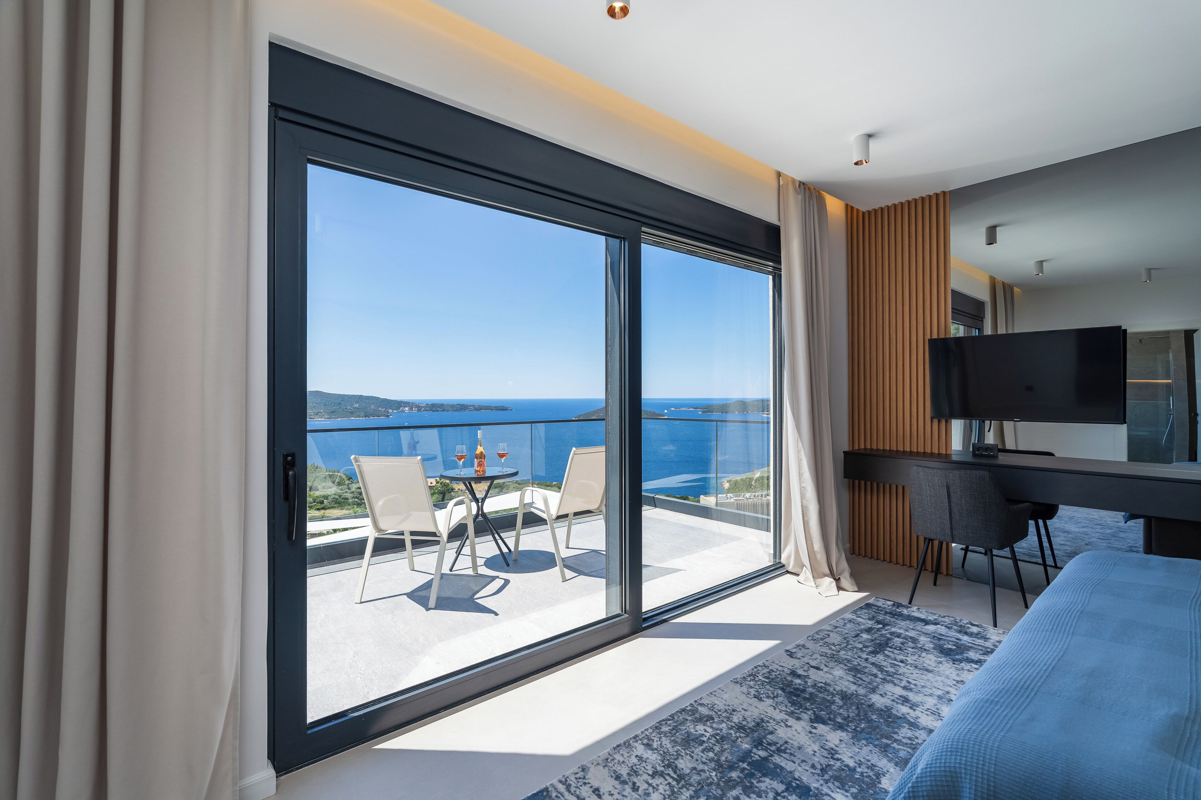 Una habitación de hotel moderna con un gran ventanal corredero que da a un balcón con vistas al mar.