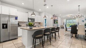 A modern kitchen with a central island, stainless steel appliances, pendant lighting, and a dining area with bar stools.
