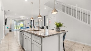 A modern kitchen with a central island, pendant lighting, and a staircase leading to another level.