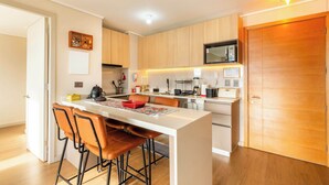 A modern kitchen with wooden cabinets, a central island with stools, and a microwave above the island.