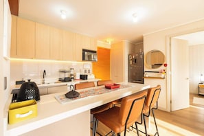A modern kitchen with wooden cabinets, a central island with seating, a refrigerator, and a microwave.
