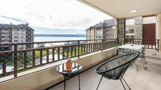 A balcony with a table and chairs, a small house model, and a view of buildings and water.