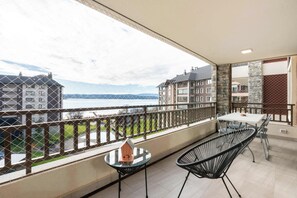 A balcony with a table and chairs, a small house model, and a view of buildings and water.