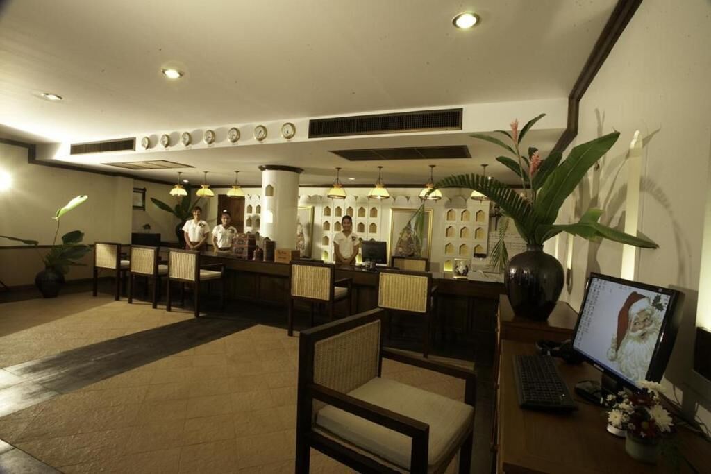 A hotel lobby with a reception desk, several chairs, a computer, and decorative plants.