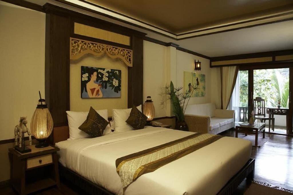 A hotel room with a large bed, a nightstand with a lamp, a painting, and a view of the outdoors.