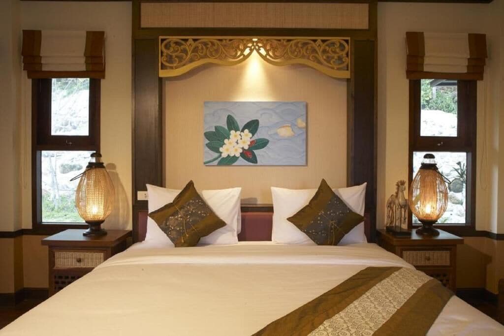 A hotel room with a large bed, two nightstands, a wall-mounted artwork, and windows with curtains.
