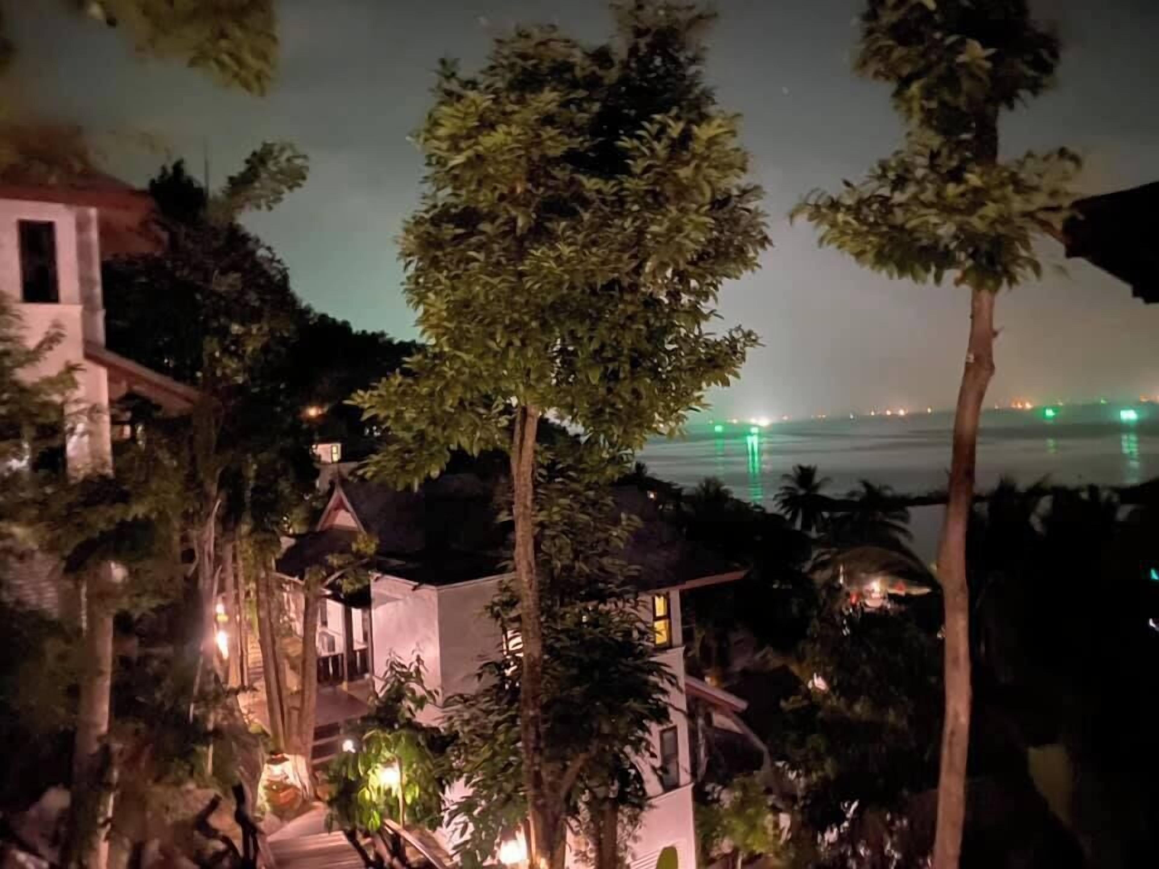 A nighttime view of a coastal property with a house surrounded by trees and a view of the sea.