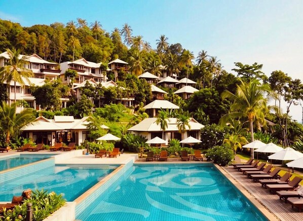 A resort with multiple swimming pools, lounge areas, and villas surrounded by lush greenery.