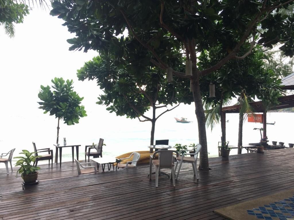 An outdoor seating area with wooden flooring, chairs, and tables, overlooking a body of water.